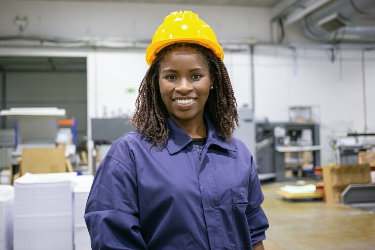 cheerful-african-american-female-factory-employee-hardhat-overall-standing-plant-floor-looking-front-smiling_74855-16344